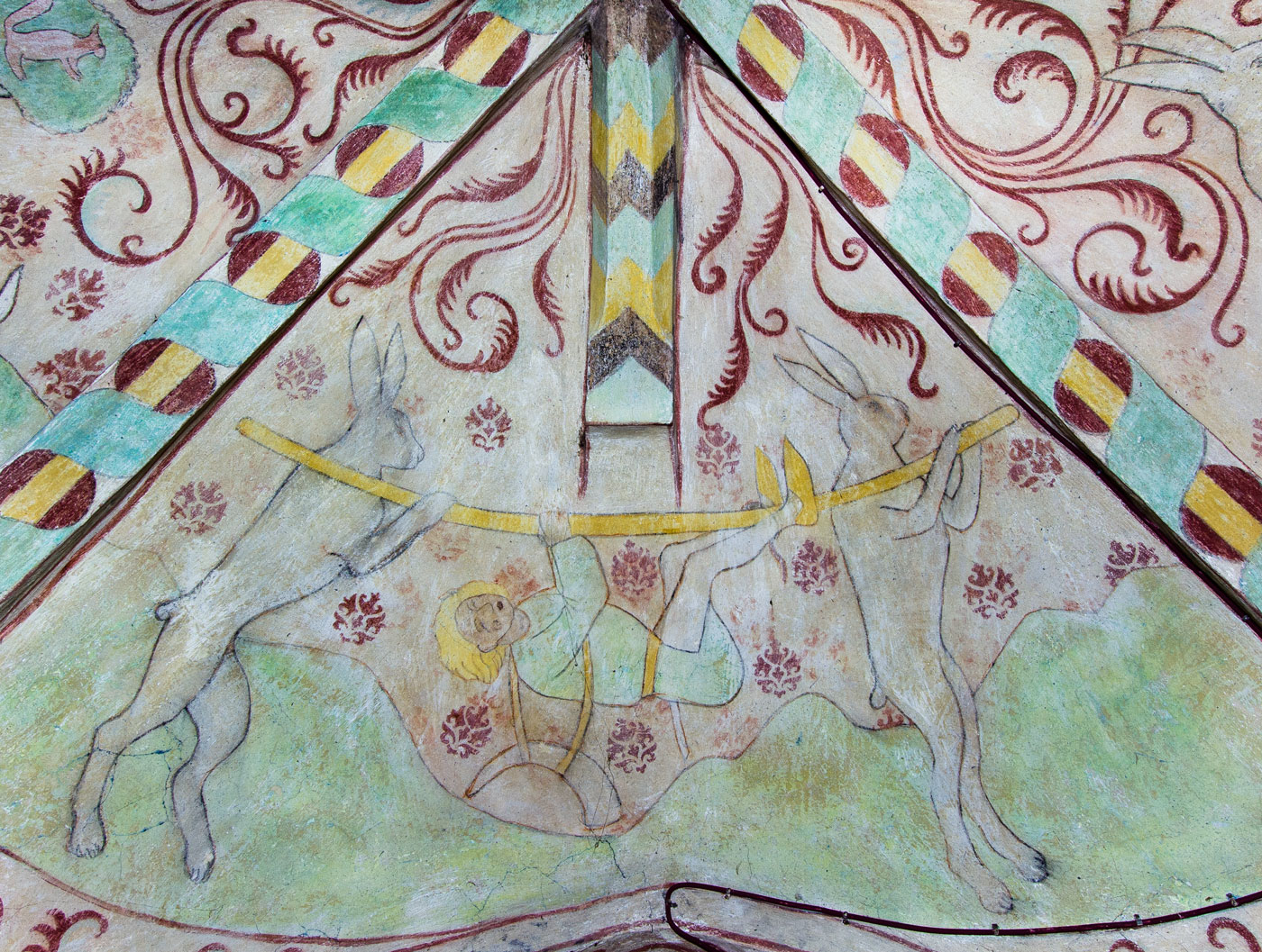 Två harar bär en stång, på vilken jägaren hänger fastbunden (S) - Kumla kyrka