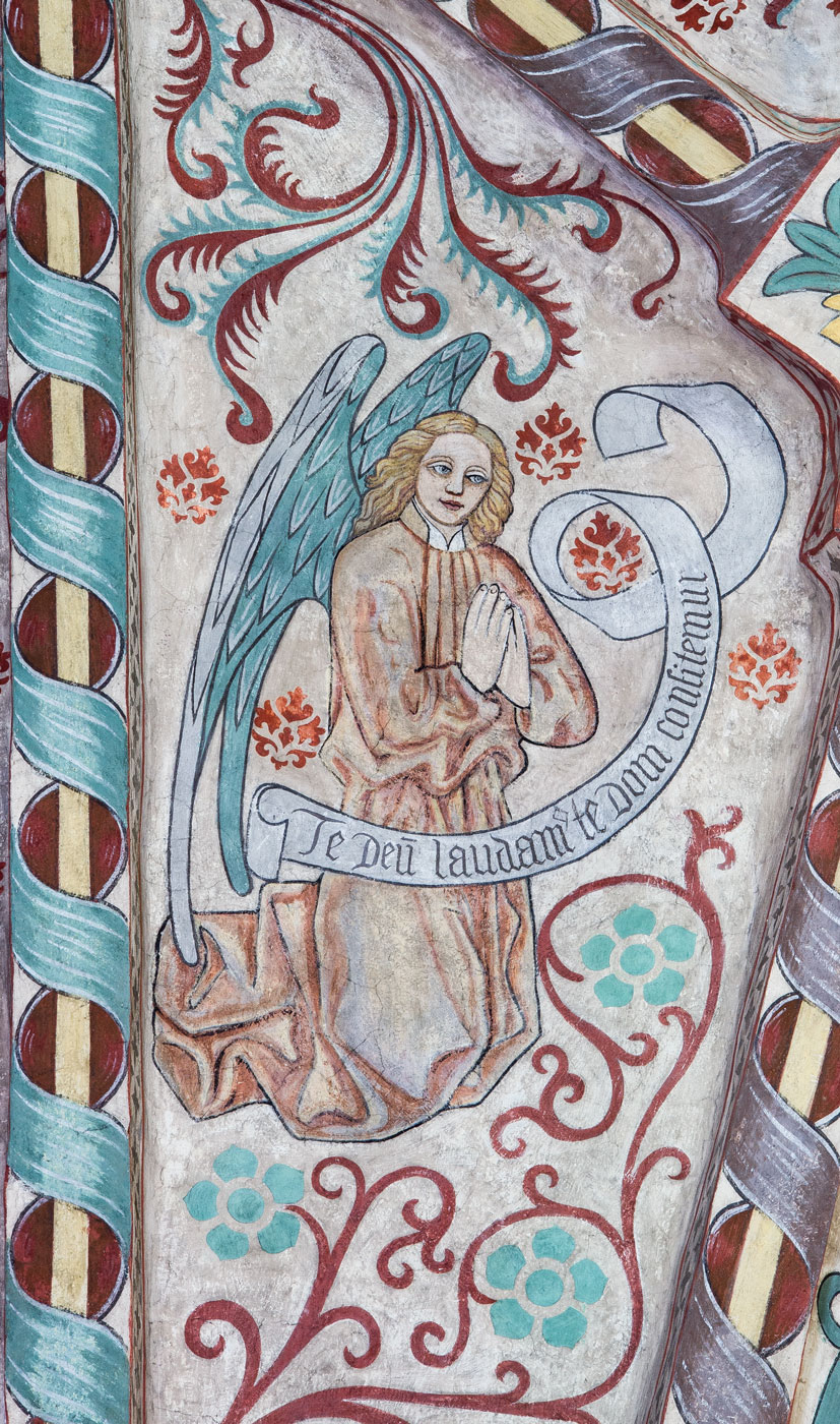 En av åtta änglar med hymnen Te Deum uppdelad på åtta språkband: Te Deum laudamus, te Dom(inum) confitemur (N) - Vittinge kyrka
